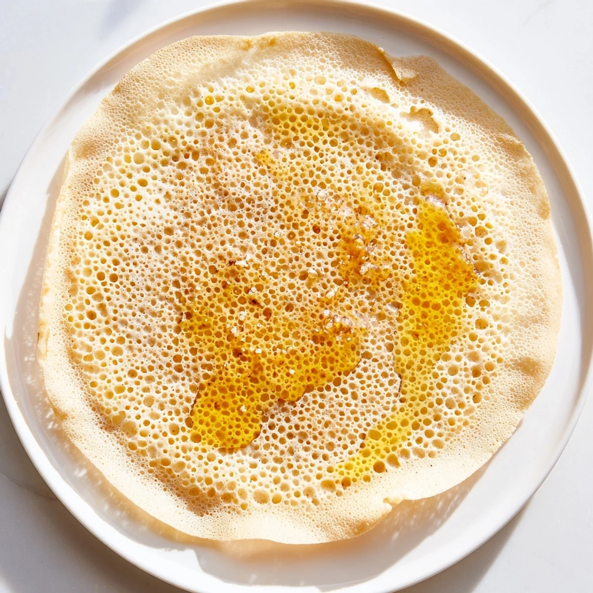 Golden-brown, bubbly Moroccan Baghrir crepes are piled high, drenched in luscious butter and honey glaze now.