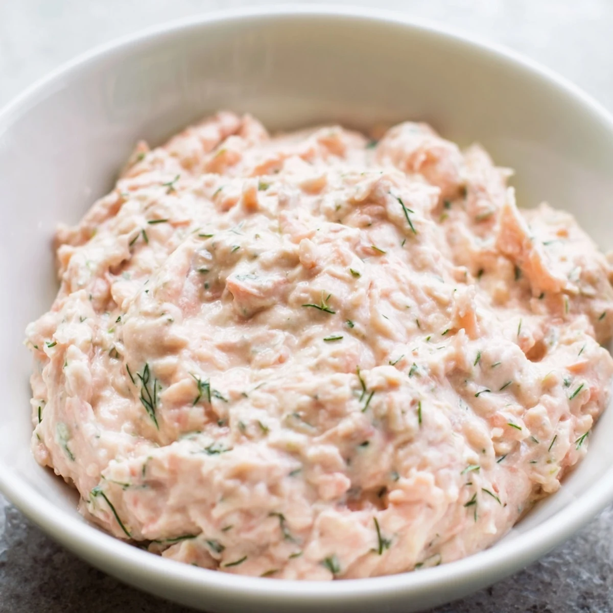 Smooth, pink smoked salmon dip spread on a crispy bagel chip, topped with a sprig of dill for a perfect appetizer bite.