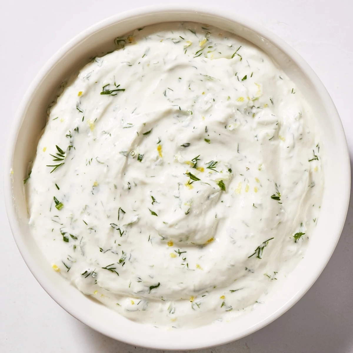 A bowl of tangy Greek Yogurt Herb Dip, garnished with lemon zest, perfect for spreading on sandwiches or dipping veggies.  