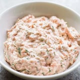 Smooth, pink smoked salmon dip spread on a crispy bagel chip, topped with a sprig of dill for a perfect appetizer bite.