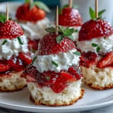 Stacked mini strawberry shortcake bites on skewers with fresh cream and berries.
