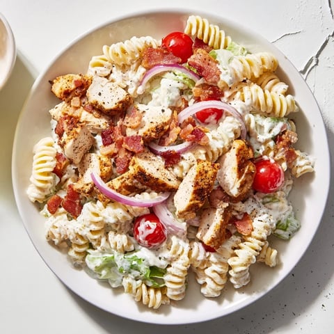 A vibrant bowl of Chicken Caesar Pasta Salad with fresh romaine and crispy bacon.