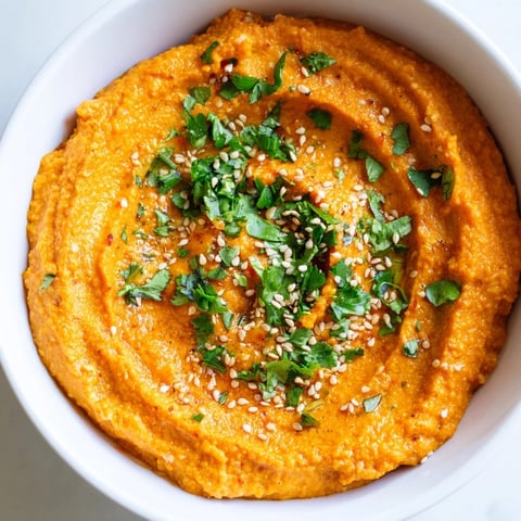 A vibrant bowl of Carrot Ginger Dip garnished with cilantro and sesame seeds, ready for dipping with crisp veggies.