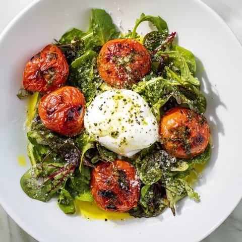 Delicious, sizzling Charred Tomato Salad with fresh greens, burrata, and basil oil dripping.
