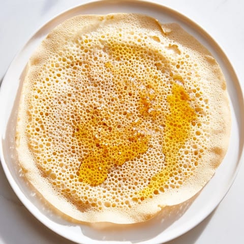 Golden-brown, bubbly Moroccan Baghrir crepes are piled high, drenched in luscious butter and honey glaze now.