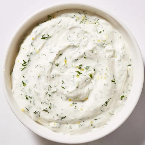 A bowl of tangy Greek Yogurt Herb Dip, garnished with lemon zest, perfect for spreading on sandwiches or dipping veggies.  