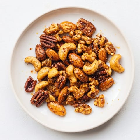Spiced nuts mix roasted to perfection, served warm in a rustic dish, perfect for snacking or adding to a cheese board.  