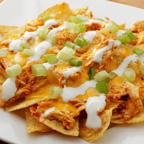 Crisp tortilla chips layered with spicy buffalo chicken and Monterey Jack cheese, finished with fresh cilantro and diced tomatoes for a game-day snack.