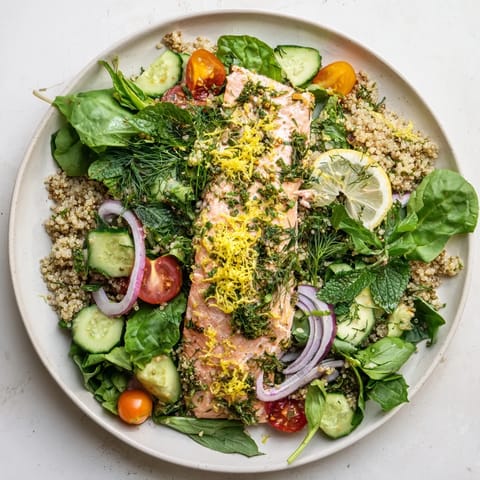 Warm Lemon Herb Salmon Salad features tender salmon fillets over fluffy quinoa, crisp vegetables, and vibrant herbs on a white plate.