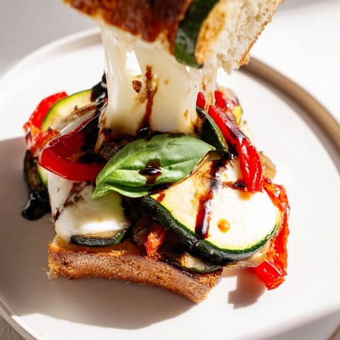 A close-up view shows melted mozzarella oozing from the golden-brown bread of a Roasted Veggie Caprese Grilled Cheese sandwich.