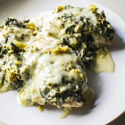 Fork cutting into juicy Spinach & Artichoke Chicken Bake, revealing a rich, tangy Greek yogurt and spinach layer.
