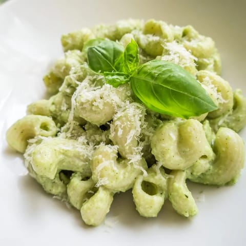 A close-up view of creamy avocado pesto mac in a white bowl, showcasing the vibrant sauce clinging to every tender noodle.  