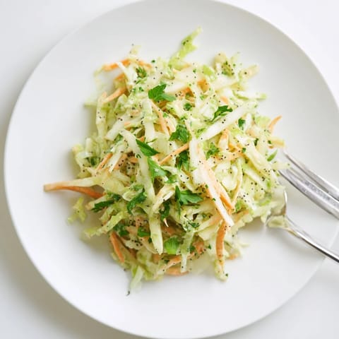 Bright green cabbage, shredded carrots, and crisp tart apple slices tossed in a creamy tangy dressing in a white bowl.