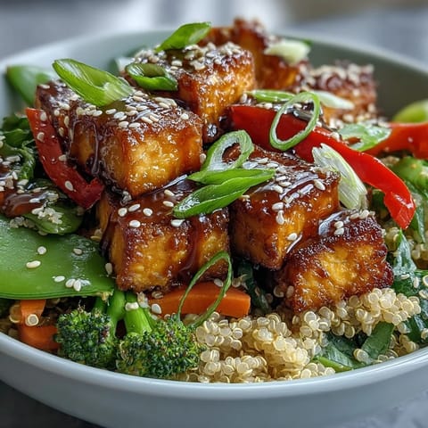 Fluffy quinoa and crispy tofu pieces topped with colorful stir-fried vegetables, all coated in a glossy teriyaki sauce in a ceramic bowl.