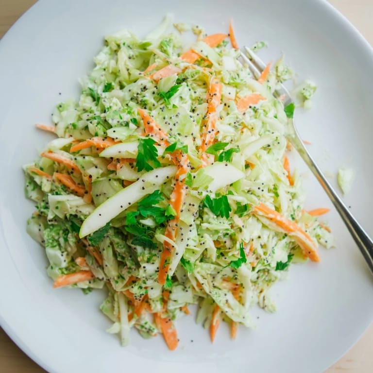 A close-up view of a refreshing Green Cabbage and Apple Slaw topped with fresh parsley and poppy seeds.